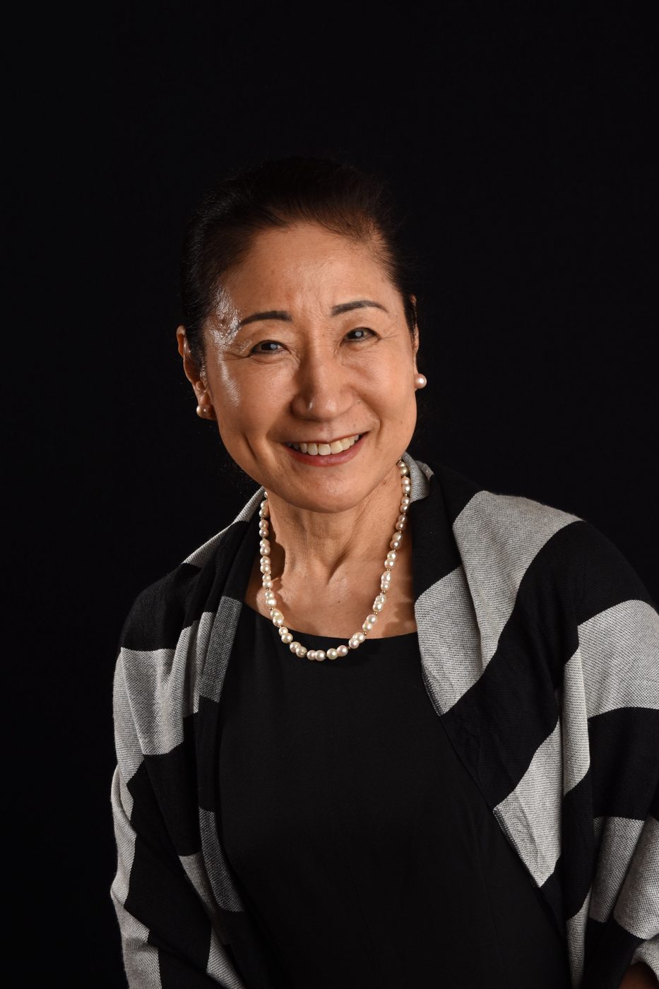 Retrato de estúdio de mulher sorrindo, com colar de pérolas e fundo preto